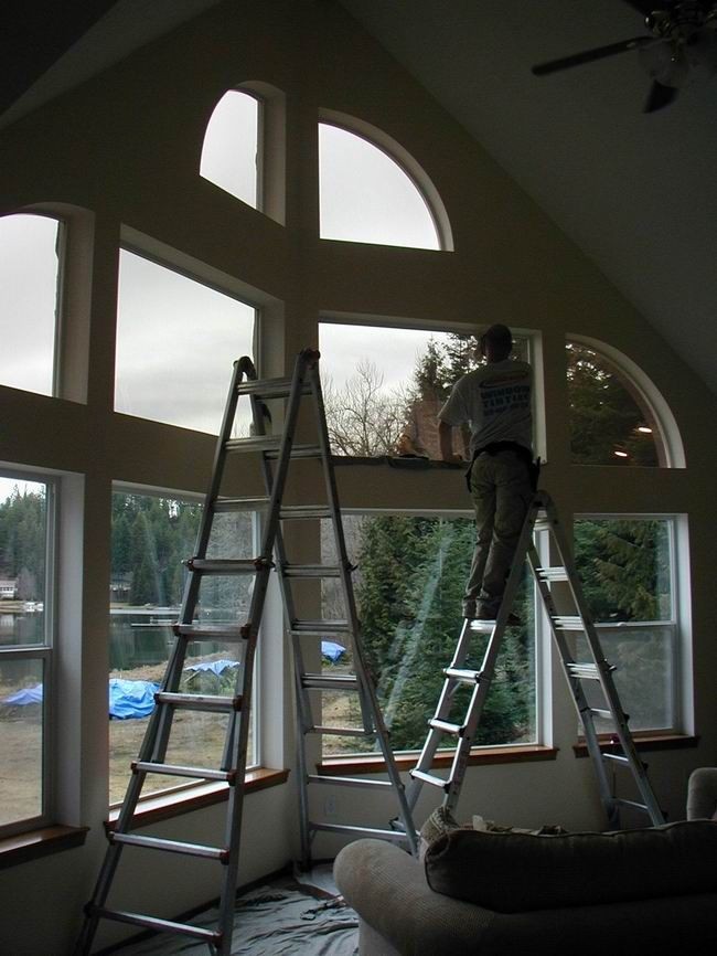 Person standing on a ladder cleaning large curved windows with a scenic view outside.