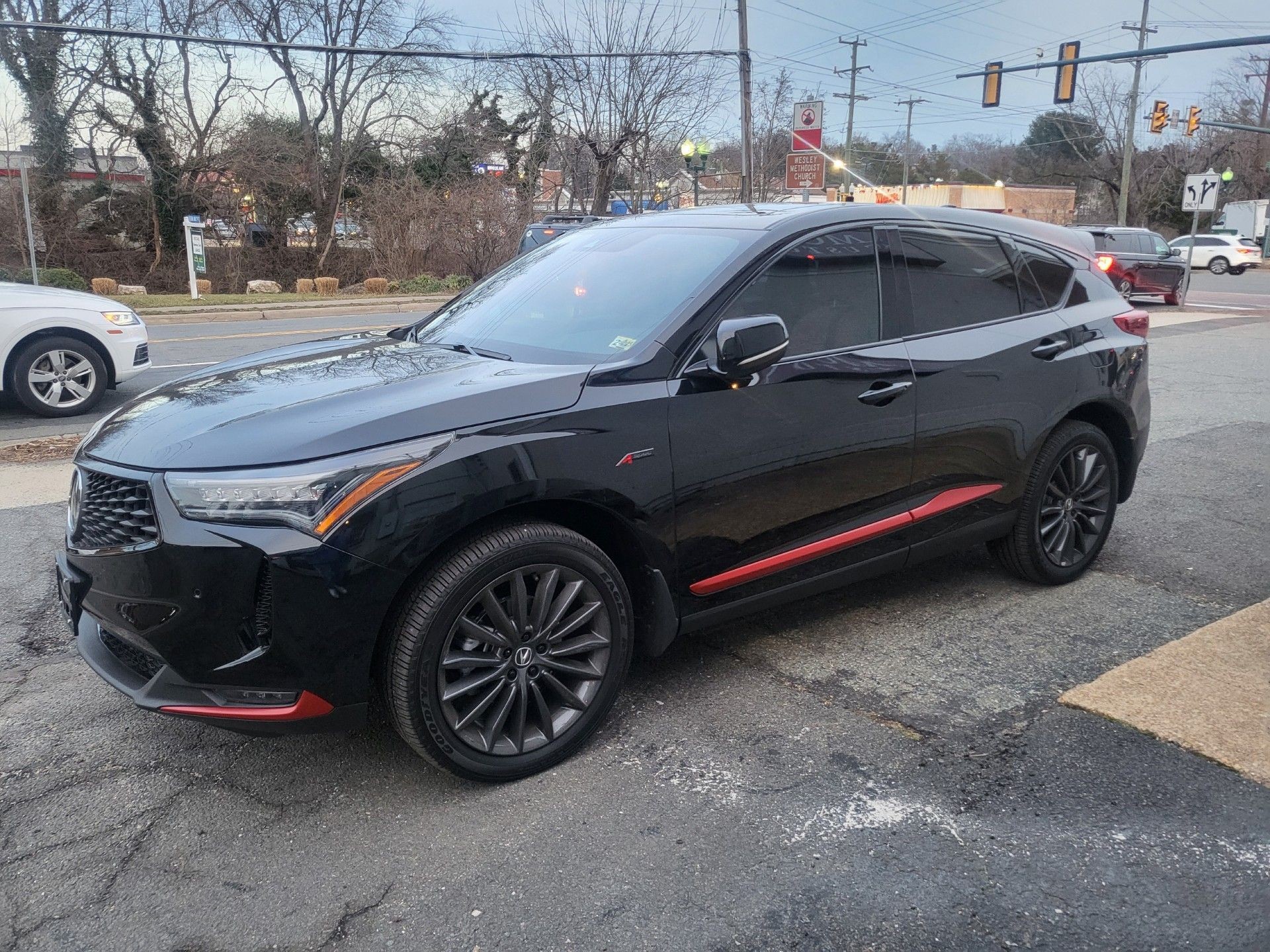 Black SUV with tinted windows parked on a street by trees and traffic lights.